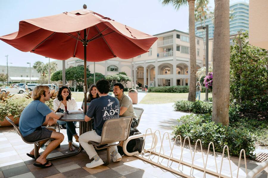 Intercultural studies students sit under an umbrella on campus.